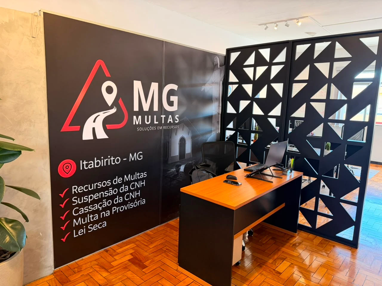 Recepção do escritório da MG Multas em Itabirito, com painel da marca listando recursos de multas, suspensão e cassação da CNH